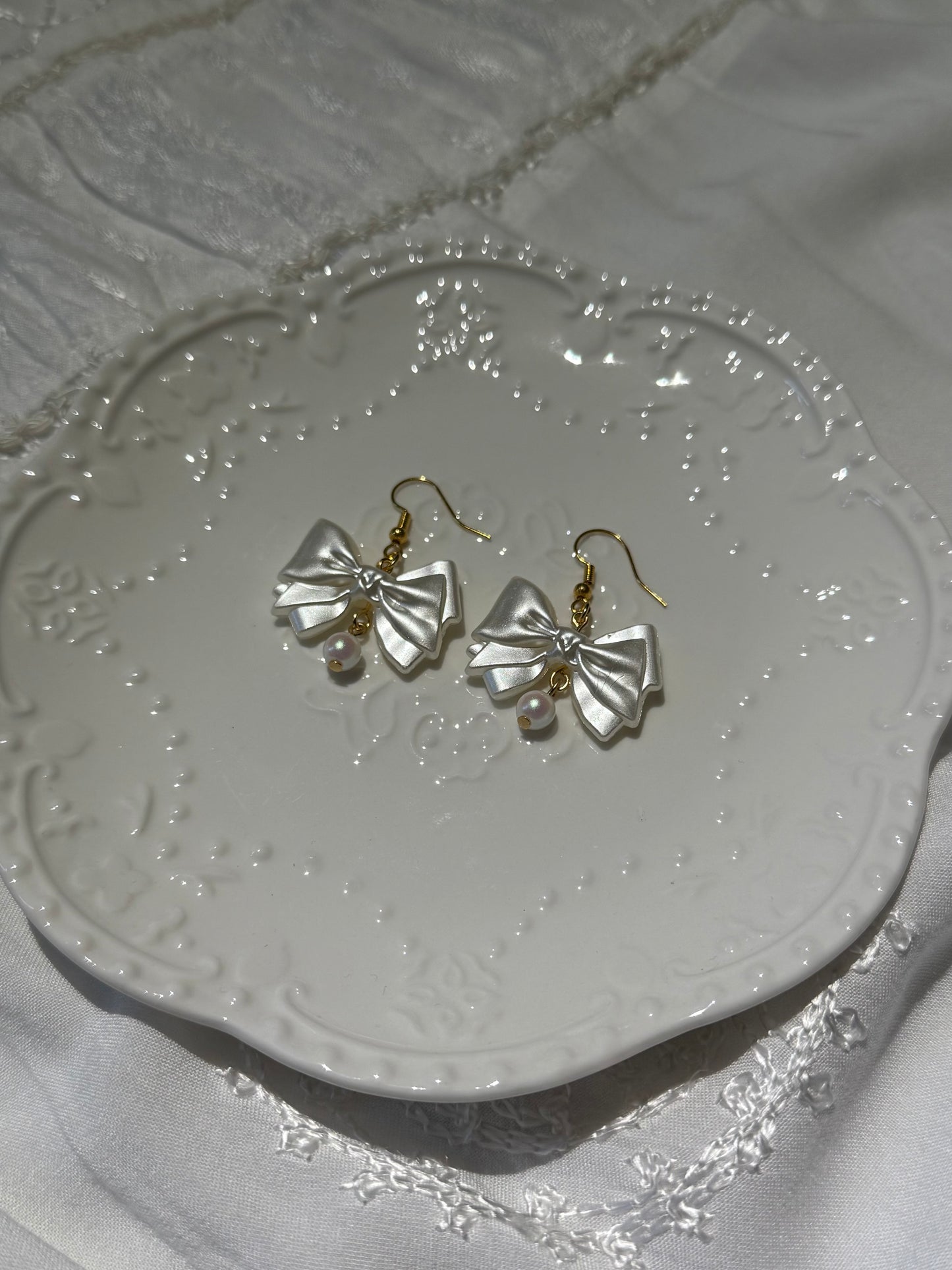 Pair of gold bow-shaped earrings on a decorative white plate.