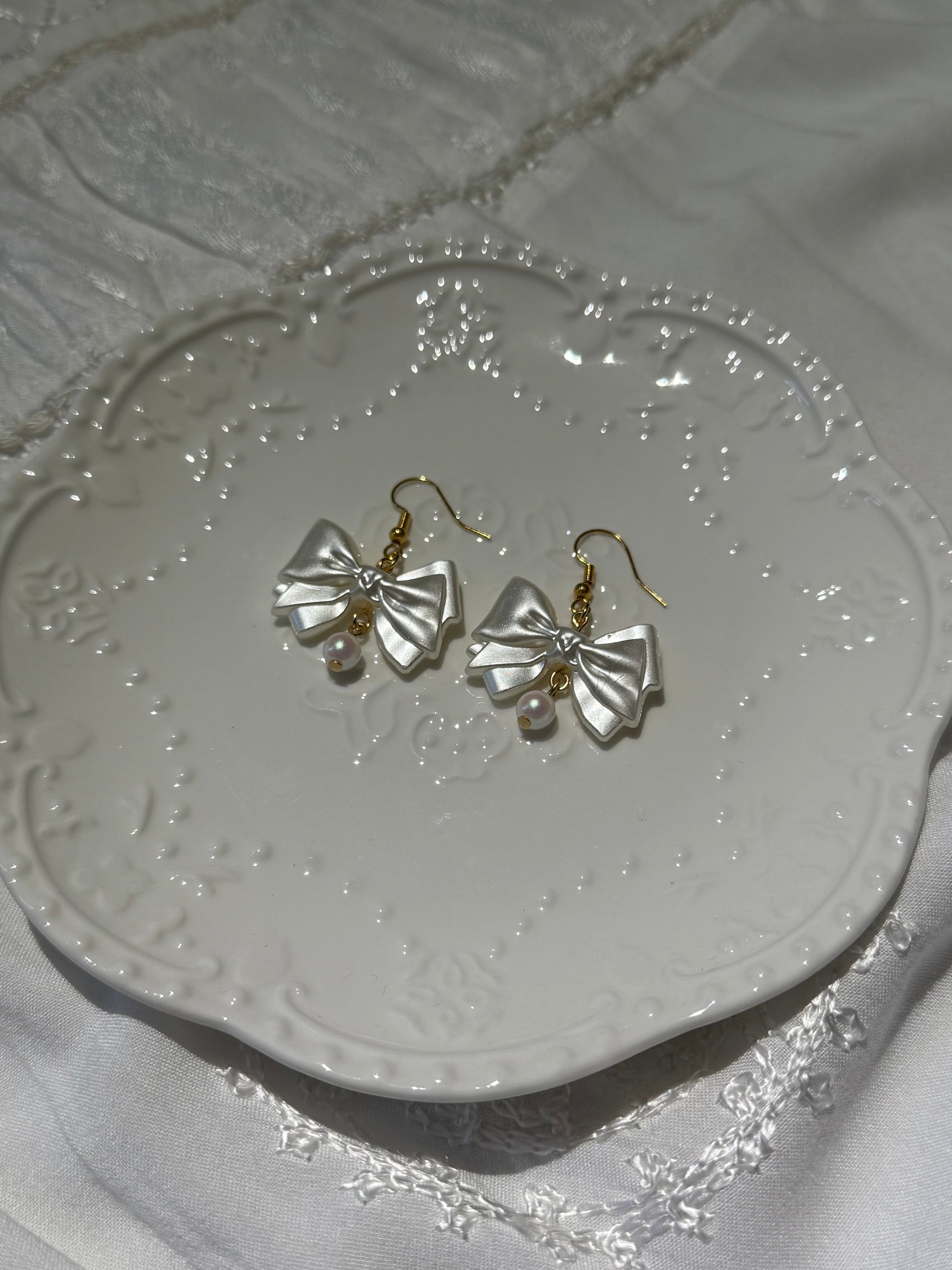 Pair of gold bow-shaped earrings on a decorative white plate.